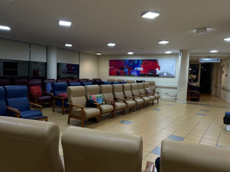 Sala de convivência iluminada com várias poltronas e um painel de arte colorido no Lar João Gonçalves Palmeiro Novo